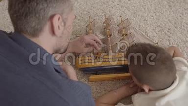 父亲和儿子躺在地板上的毛茸茸的地毯上玩船模特写。 家庭<strong>开支</strong>